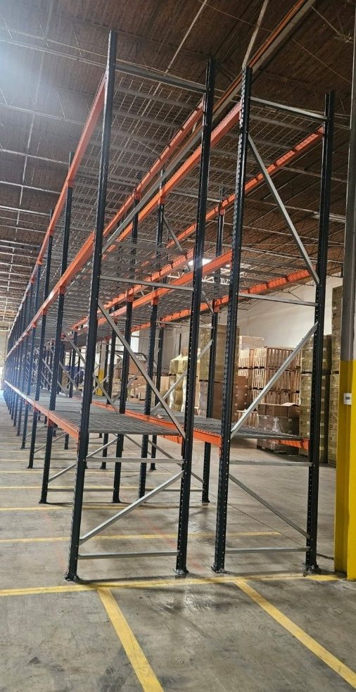 Tall selective rack frames with wire decking along the warehouse wall